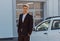 Young male consultant in auto show standing near cars and looking at camera