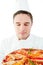 Young male cook smelling at pizza with closed eyes
