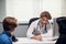 A young male doctor receiving a teen patient with his parent at the office, he is asking questions and taking notes