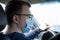 a young male driver is sitting in a car wearing a medical mask. view from the back seat of the car. self-defense against the virus