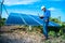 Young male engineer with laptop in hand standing near solar panels, agriculture farm land with clear blue sky background,