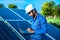 Young male engineer with laptop in hand standing near solar panels, agriculture farm land with clear blue sky background,