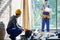 Young male engineer working at cottage construction site, picking instrument from toolbox with blurred colleague in the