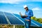 Young male engineer working on laptop standing near solar panels, agriculture farm land with clear blue sky background, Renewable