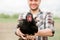 A young male farmer with a chicken in his hands stands in his garden in the village