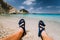 Young male feets wear blue flip-flop sandal sunbathing on sea beach with clear water