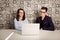 Young male and female business partners sitting behind a computer monitor and thinking of something