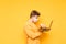 Young male freelancer in a medical gauze mask on his face enjoys a laptop on a yellow background, photo in profile. Work online in