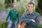 Young male gardener posing with older colleague at background