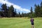 A young male golfer playing alone, standing in the middle of the fairway measuring his distance, surrounded by forest