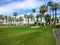 A young male golfer walking towards the green on a par 4 surrounded by water and palm trees in the background on the desert oasis