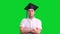 Young male graduate in black hat on green chroma key background