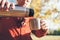 Young male hands pouring a hot tea into cup . from thermos flask in autumn forest close up image