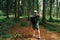 Young male hiker with a backpack stands in a mountain untouched forest and takes a photo on a smartphone camera  rear view. Guy on