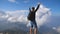Young male hiker reaching up top of mountain and raising arms. Man enjoying freedom during summer travel. Cloudy sky at