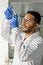 Young male laboratory worker looking at flask containing green lab-grown sprout