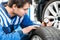 Young Male Mechanic Pressing Gauge Into Tire In Garage