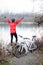 Young male mountain biker standing by the river or lake with arms raised in the air, celebrating success