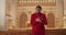 Young male musician in red clothes looking to camera and singing while standing at row of wooden pews. Joyfull guy