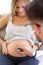 Young male obstetrician doctor with stethoscope listening to beautiful pregnant woman baby heartbeat.