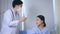 Young male otolaryngologist with stethoscope examining Asian female patient in uniform using tympanic thermometer for