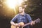 Young male in a park holding a guitar and playing a song from the Christian hymn book