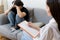 Young male patient sitting on sofa consulting with female psychologist.