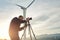 Young male photographer shoots video on digital camera while standing against wind turbine in countryside