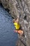 Young male rock climber hanging over the water and