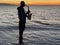 Young male saxophonist stands with his feet in sea water, holds saxophone in his hands, looks at sunset. Beautiful sunset on sea,