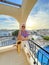 A young male saxophonist in white pants and a purple T-shirt stands on the balcony of a hotel in Cyprus and holds a saxophone