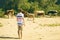 Young male shepherd walking near the cow herd on the summer sandy field a