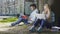 Young male sitting under tree with book near female with laptop, student life