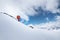 Young male skier in an orange suit rushes at speed along a snowy slope against the backdrop of high snow-capped