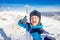 Young male skier smiling makes selfie photo on background of winter ski resort in protective helmet, sunny day, blue sky