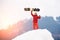 Young male snowboarder standing on the top of the snowy hill with, holding snowboard in hand above head