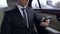 Young male in suit texting on smartphone while riding in personal business car