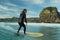 A young male surfer in a black wetsuit rides a longboard surfboard on a wave in front of Lion Rock, Piha Beach, New Zealand