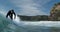 A young male surfer rides a surfboard on a wave in front of Lion Rock at Piha Beach, Auckland, New Zealand