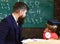 Young male teacher guides his child student to learning while son looks at chalkboard with scribbles on, sitting in