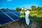 Young male technician worker wearing green vests and helmet checks the maintenance of the solar panels and talking about