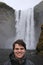 Young male tourist aged 20-25 poses in front of skogafoss waterfall in Iceland. Iceland has become a popular tourist