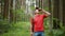 Young male tourist with a backpack drinks from a flask standing in a dark forest, tracking the camera