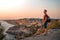 A young male tourist with a backpack stands on the shore high above the sea at sunset and admires Cape Fiolent in the Crimea