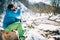 Young male tourist drinks hot coffee from a thermos near a river in the mountains.