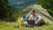 A young male tourist uses a laptop in a camping near a tent. In a picturesque place in the background of the mountains