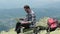 Young male traveler working on laptop outdoors on top of mountain.