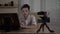Young male video vlogger filming himself with a camera at office teaching audience how to start an online blog -
