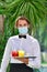 A young male waiter with a surgical mask outdoors holding a bar tray with assorted drinks