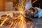 A young male welder in a white working gloves grinds a metal product with angle grinder in the garage